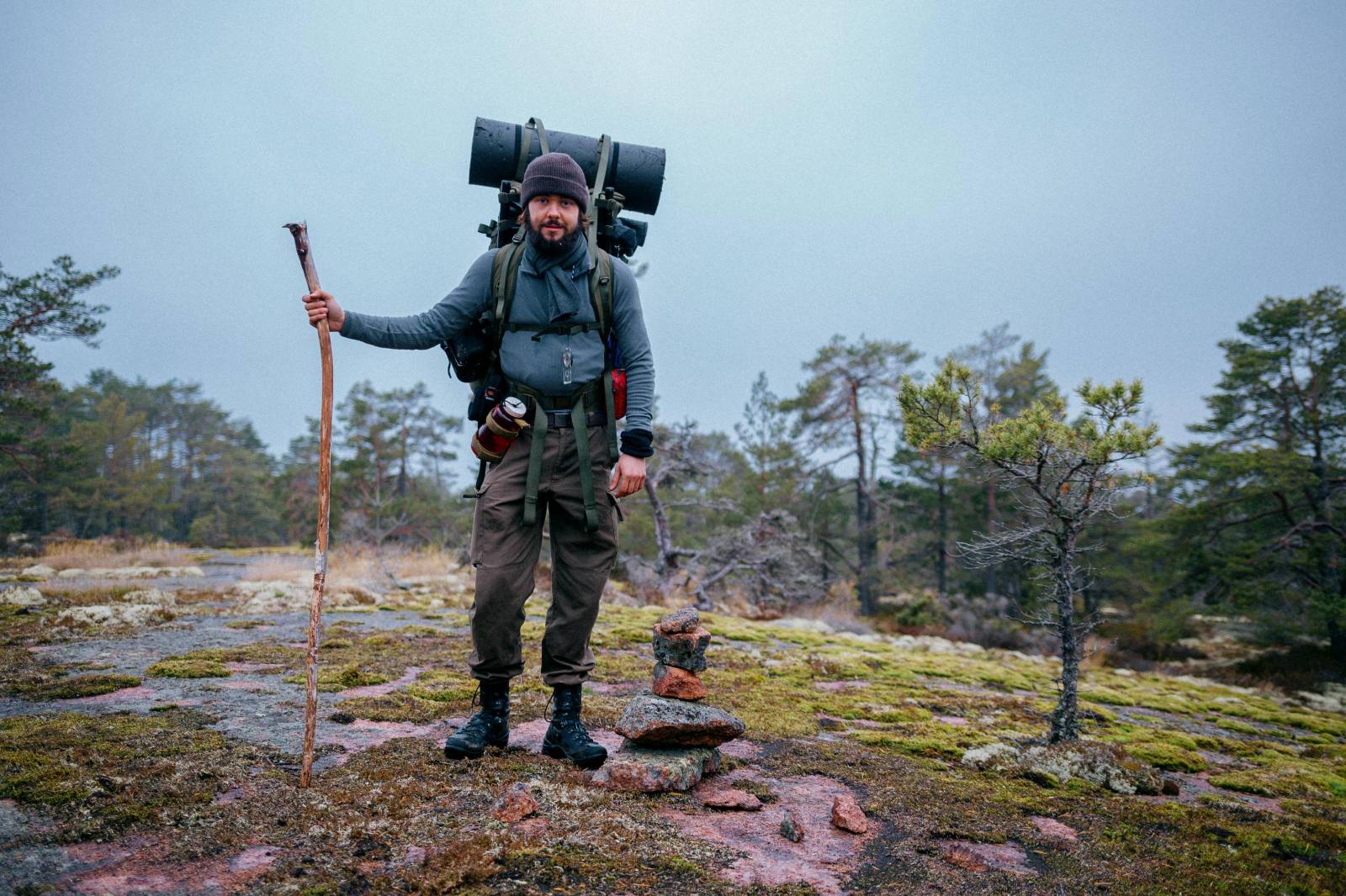 Photo of a hiker standing on the rock in the forest with a hiking pole out of a tree branch.